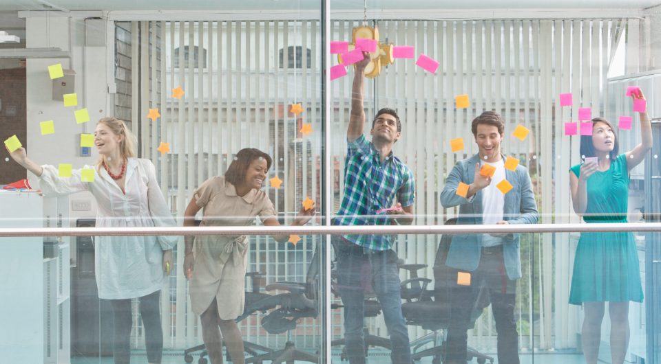 Excited business people with arms raised at window covered in adhesive notes
